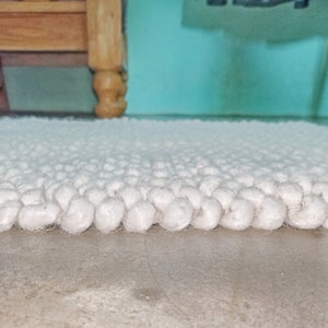 Puede incluir: Primer plano de una alfombra blanca y esponjosa con una superficie texturizada. La alfombra est&aacute; hecha de peque&ntilde;as bolas redondas de hilo.