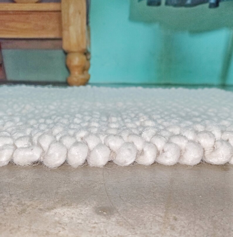 Puede incluir: Primer plano de una alfombra blanca y esponjosa con una superficie texturizada. La alfombra est&aacute; hecha de peque&ntilde;as bolas redondas de hilo.