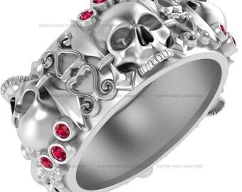 May include: A silver skull ring with red gemstones and intricate details. The ring features a skull with a crown and a heart design.