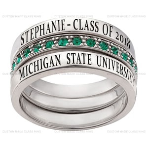May include: A silver ring with a green gem stone band. The ring has the words "Stephanie - Class of 2018" and "Michigan State University" engraved on it.