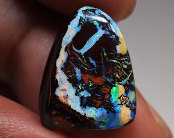 May include: A polished, teardrop-shaped opal displays a vibrant play of color. The gemstone features a dark brown base with swirling patterns of blue, green, and orange, and a creamy white edge. The opal's surface is smooth and reflective.