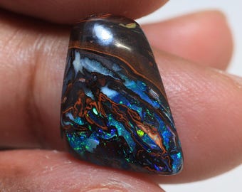 May include: A dark brown, blue, and green opal gemstone with a rough, irregular shape. The opal has a unique pattern of swirling colors and a high shine.