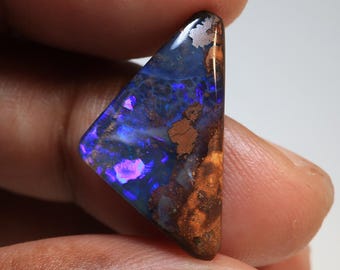 May include: A triangular-shaped opal gemstone with a polished surface. The stone displays a vibrant play of color, with blues, purples, and flashes of pink. Brown and orange matrix patterns are visible on the surface.