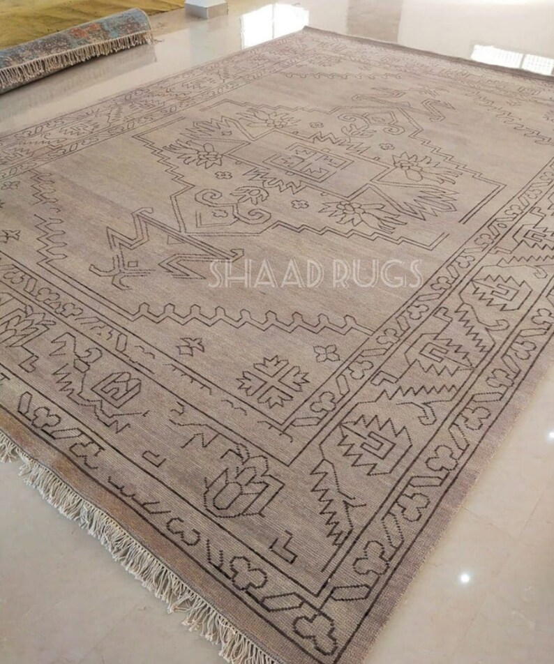 May include: A beige rug with a brown geometric pattern. The rug has a fringe border and is made of wool. The rug is called "Shaad Rugs".