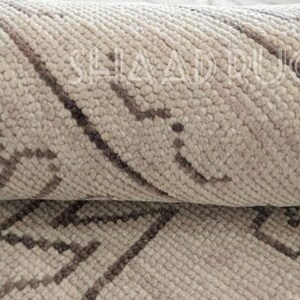 May include: Close-up of a beige and brown patterned rug with a woven texture. The rug has a geometric design with diagonal lines and small squares.