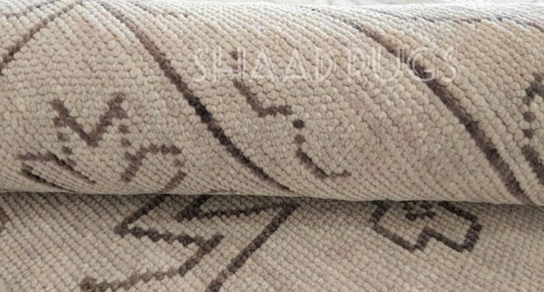 May include: Close-up of a beige and brown patterned rug with a woven texture. The rug has a geometric design with diagonal lines and small squares.