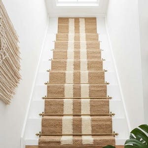 May include: Staircase with white risers and brown and cream striped stair runners. Woven wall decor and three woven baskets hang on the white wall. A large green leaf is in the bottom right corner.
