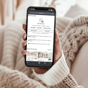 A person is holding a smartphone displaying a webpage with information about a seller named ArtNebal.