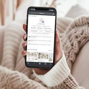 A person is holding a smartphone displaying a webpage with information about a seller named ArtNebal.