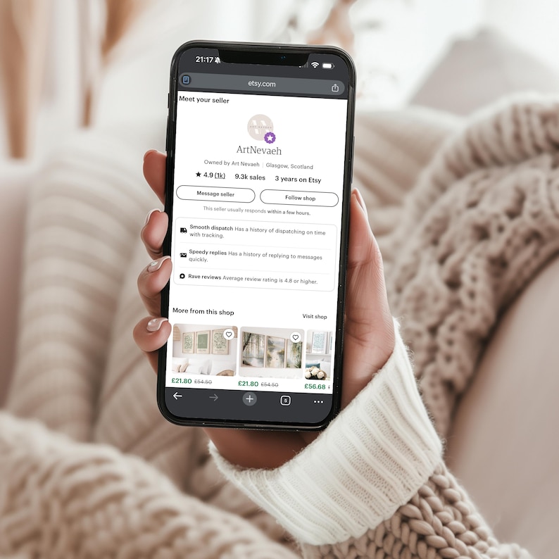 A person is holding a smartphone displaying a webpage with information about a seller named ArtNebal.