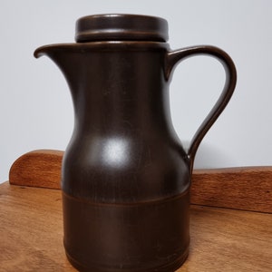 May include: A brown ceramic jug with a lid and a handle. The jug has a smooth, glossy finish.