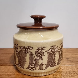 May include: A brown and cream ceramic jar with a lid. The jar has a brown and white fruit design around the middle.