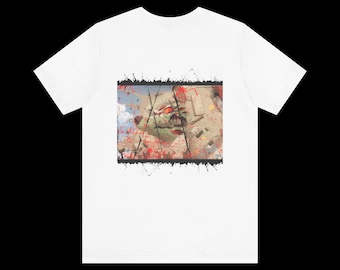 May include: White t-shirt with a graphic print of a colorful, abstract design with red, white, and black accents. The design features a cracked, textured surface with a green and white figure.