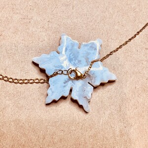 May include: A white snowflake pendant necklace with a gold chain. The snowflake is made of a white material with a marbled effect. The chain is a delicate gold chain with a lobster clasp.