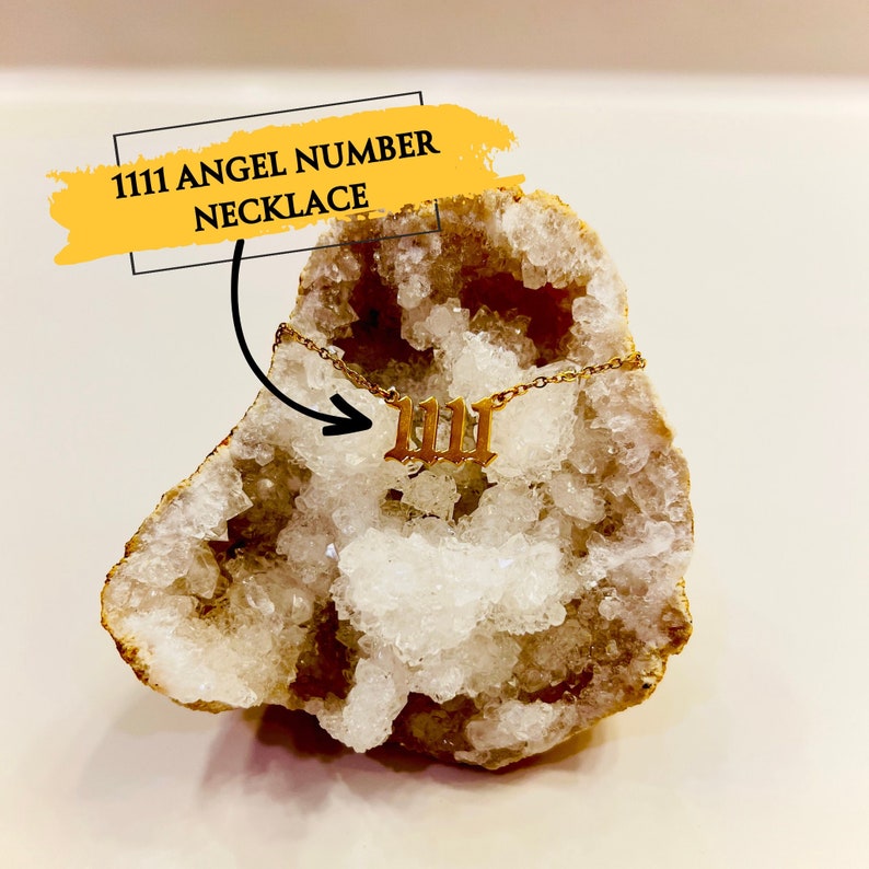 May include: Gold necklace with the number 1111 in a gothic font. The necklace is displayed on a white crystal geode. The text "1111 ANGEL NUMBER NECKLACE" is written in yellow on a white background.