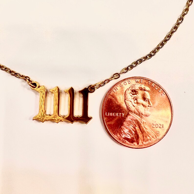 May include: Gold chain necklace with a pendant featuring the Roman numeral 'III' in a gothic font. The pendant is shown next to a US penny for size comparison.