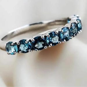 Può includere: Un anello a fascia d'argento con una fila di pietre preziose blu. L'anello è incastonato con un totale di 10 pietre rotonde.