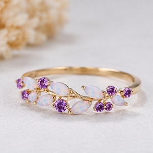 Peut inclure: Une bague en or au design délicat inspiré de la vigne, ornée d'opales irisées taille marquise et de pierres précieuses violettes taille ronde. L'anneau est en or poli et les pierres sont disposées en un motif symétrique rappelant des feuilles.