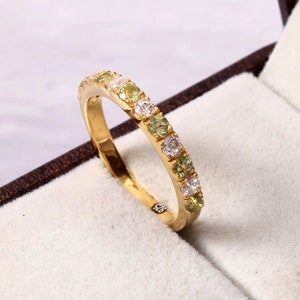 May include: A gold band ring with alternating green and white gemstones.
