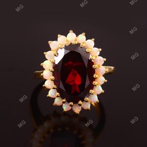May include: A gold ring featuring a large oval red gemstone encircled by a halo of small white gemstones.