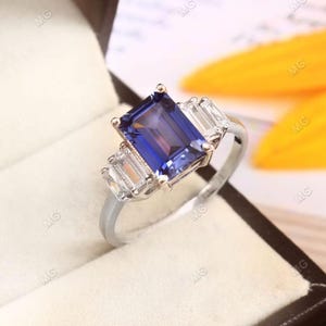 May include: A silver ring featuring a large, rectangular, dark blue gemstone surrounded by three smaller, rectangular, clear gemstones.