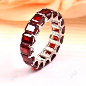 May include: A silver band ring with a row of red square-shaped gemstones.