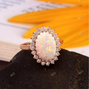 Puede incluir: Un anillo de oro rosa con una gran opala ovalada rodeada por un halo de diamantes más pequeños.