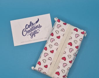 May include: A white tissue box cover patterned with pink and red hearts. A business card with the text "Cole Creations Gifts" and the website address is also visible. The background is a solid blue.