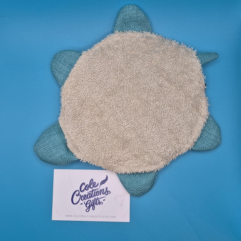 May include: A turtle-shaped bath mat with a light gray center and teal flipper-like edges. The mat is made of a soft, absorbent material. A white card with the text "Cole Creations Gifts" is at the bottom.