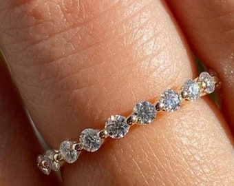 May include: A gold band ring with a series of round, clear gemstones set along the top. The ring is shown on a finger, with the gemstones catching the light. The ring is a delicate piece of jewelry.