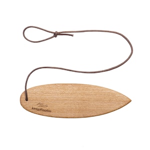 Könnte beinhalten: Ein Holz-Surfbrett-Schlüsselanhänger mit einem braunen Lederband. Der Schlüsselanhänger trägt die Gravur "keepfloatin".