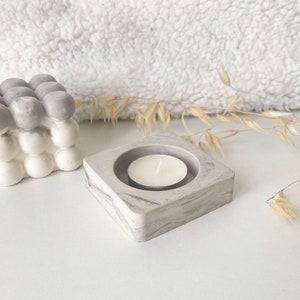 Peut inclure: Un bougeoir carré en marbre gris avec une dépression ronde au centre pour accueillir une petite bougie chauffe-plat blanche.