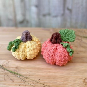 May include: Two crocheted pumpkins, one yellow and one peach, with green leaves.