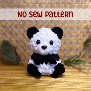 May include: No Sew Pattern - A white and black plush panda bear toy with black eyes and a black nose. The panda is sitting on a wooden surface.