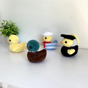 May include: Four handmade crochet ducklings in various colors and styles. One is yellow, one is teal and brown, one is a sailor duck with a white hat and red scarf, and the last is a graduate duck with a black cap and gown.