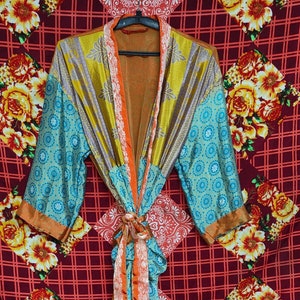 Pode incluir: Uma bata de seda azul, laranja e dourada com padrão floral. A bata tem um cinto de laço e mangas compridas.