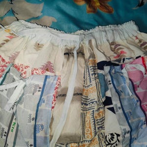 May include: A patchwork skirt with a white drawstring waist. The skirt is made of different fabrics with various patterns, including stripes, floral designs, and geometric shapes. The skirt is a mix of light blue, white, pink, and beige.
