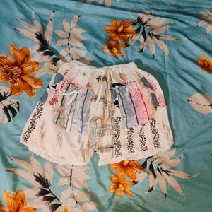 May include: A white patchwork skirt with a drawstring waist. The skirt is made of different fabrics and patterns, including floral, geometric, and striped. The skirt is a unique and stylish piece of clothing.