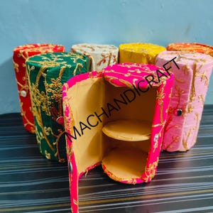 Könnte beinhalten: Ein Set aus sechs bunten zylindrischen Boxen mit gestickten Blumenmustern. Die Boxen sind geöffnet, um einen zweistufigen Innenraum zu zeigen. Die Boxen sind aus Stoff gefertigt und haben einen goldenen Rand. Die Boxen sind mit "MACHANDICRAFT" beschriftet.