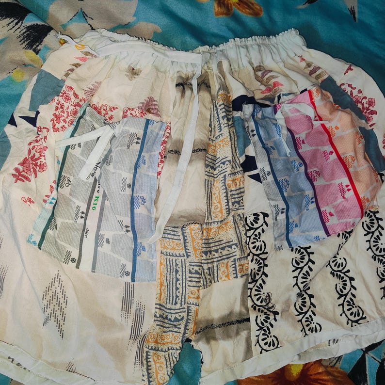 May include: A white patchwork skirt with a variety of patterns, including floral, geometric, and striped designs. The skirt has a white drawstring waist and is made of a lightweight fabric.
