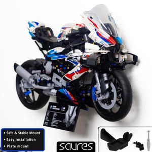 Könnte beinhalten: Ein weißes, blaues und rotes Lego-Motorradmodell, das an einer Wand mit einer schwarzen Halterung befestigt ist. Das Motorrad hat eine klare Windschutzscheibe und einen schwarzen Rahmen. Das Modell wird an einer weißen Wand mit schwarzem Hintergrund gezeigt.