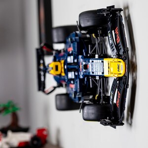 Puede incluir: Un modelo Lego azul y amarillo de un coche de carreras de F&oacute;rmula 1 con el logotipo de Red Bull en el lateral. El coche est&aacute; montado en una pared con un soporte negro.