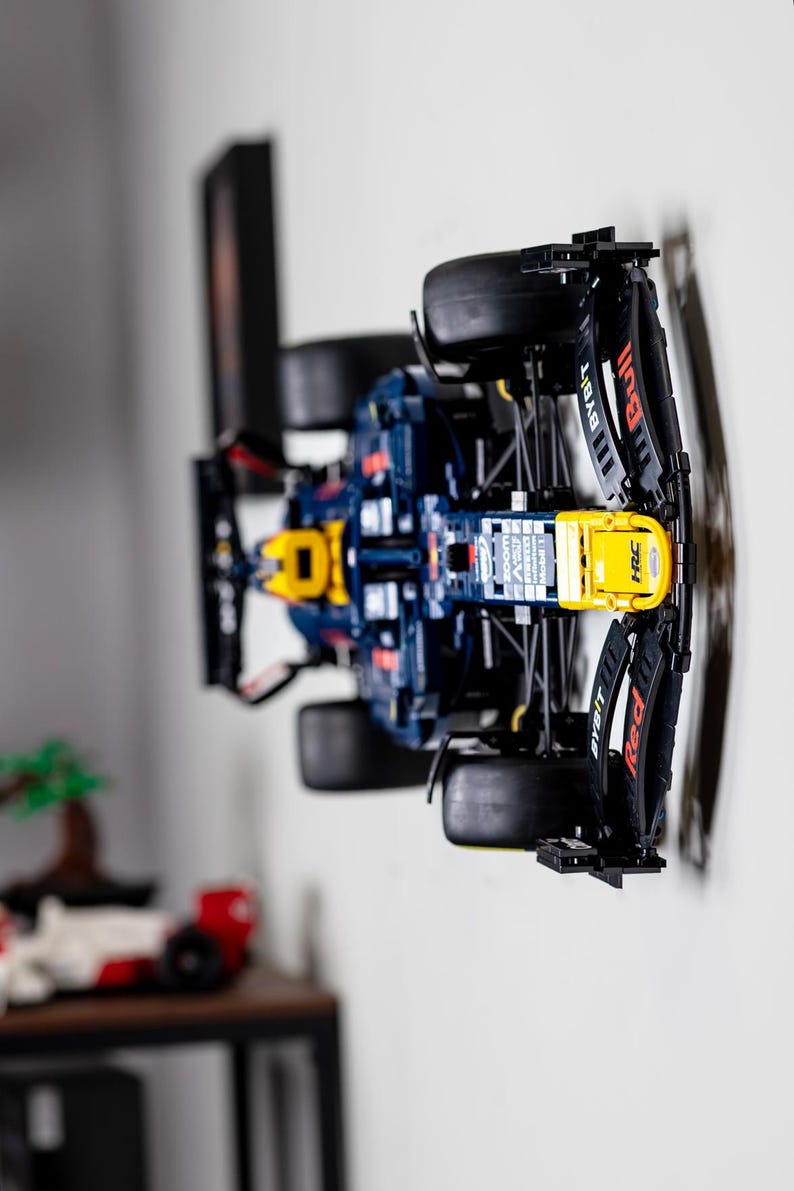 Puede incluir: Un modelo Lego azul y amarillo de un coche de carreras de F&oacute;rmula 1 con el logotipo de Red Bull en el lateral. El coche est&aacute; montado en una pared con un soporte negro.