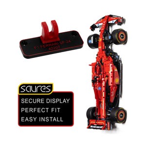 Puede incluir: Un coche de carreras de Fórmula 1 Ferrari SF-24 rojo con neumáticos negros, acompañado de un soporte de montaje rectangular negro con un clip rojo en forma de U y el texto F1 FERRARI SF-24 42207. Un letrero negro con borde amarillo muestra el texto SAURES SECURE DISPLAY PERFECT FIT EASY INSTALL.