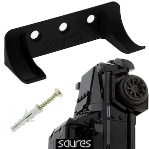 May include: Black plastic wall mount with three holes and the word "Saures" printed on it. The mount is designed to hold a toy vehicle. A black toy vehicle is shown in the background.