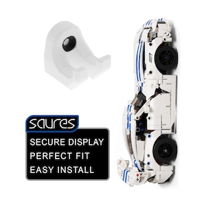 Peut inclure: Un support mural en plastique blanc pour voiture miniature, doté d'un crochet incurvé. À côté se trouve une voiture de sport miniature blanche avec des bandes bleues. Un panneau noir affiche le texte : SAURES, SECURE DISPLAY, PERFECT FIT, EASY INSTALL.