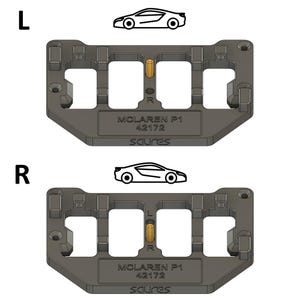 May include: A black plastic model car stand with a gold pin in the center. The stand has two rectangular openings and the text "MCLAREN P1 42172 SCURES" printed on the bottom. A white outline of a McLaren P1 car is shown above the stand.