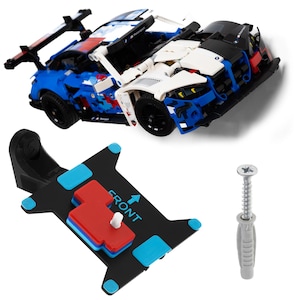May include: A blue, white, and black toy race car with a spoiler and black wheels. A black mounting bracket with blue and red accents and the word "FRONT" is also included, along with a screw and wall anchor.