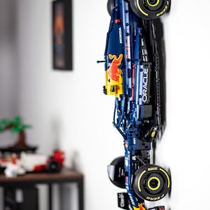 Puede incluir: Un modelo Lego azul y rojo de un coche de carreras de F&oacute;rmula 1 con el logotipo de Oracle Red Bull Racing y las palabras "Red Bull" y "Mobil 1" en el lateral. El coche est&aacute; montado en una pared con las ruedas hacia afuera.