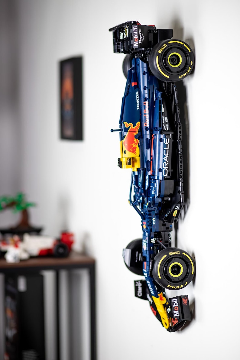 Puede incluir: Un modelo Lego azul y rojo de un coche de carreras de F&oacute;rmula 1 con el logotipo de Oracle Red Bull Racing y las palabras "Red Bull" y "Mobil 1" en el lateral. El coche est&aacute; montado en una pared con las ruedas hacia afuera.